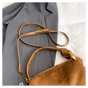 Detail of brown suede cylinder bag with gold metal rings and dual shoulder straps