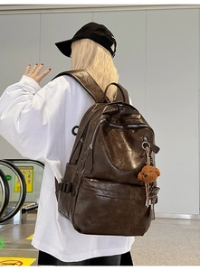 Detail of large dark brown leather backpack with multiple zippers and bear charm