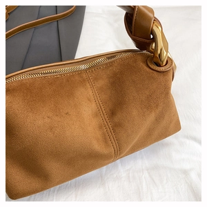 Detail view of caramel brown suede cylinder bag with gold metal ring and knotted strap