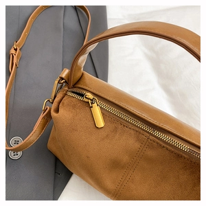 Detail of caramel cylindrical bag featuring matte leather and suede stitching with gold zipper
