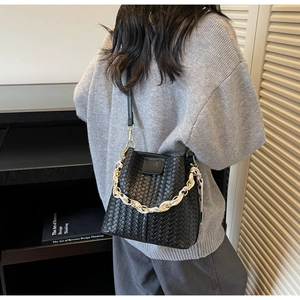 Détail du sac seau tressé noir avec chaîne en métal et foulard en soie décoratif à motifs