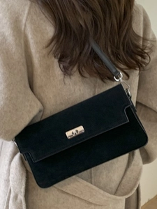 Minimalist black suede shoulder bag with silver clasp shown on model in beige coat