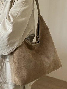 Grand sac hobo minimaliste en daim marron porté par un mannequin de profil avec un trench