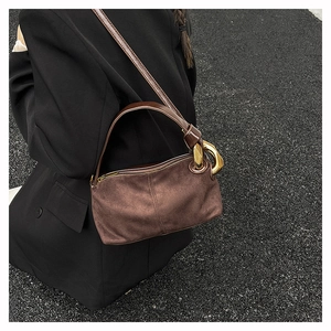 Detail of a brown suede cylinder bag with a gold metal ring buckle on a shoulder strap