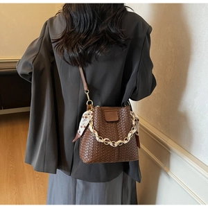 Détail d'un sac seau tressé marron orné d'un foulard en soie et d'une chaîne métal