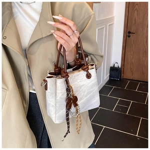 Detail of retro bucket bag with rope knot handle and bow charm held by a model