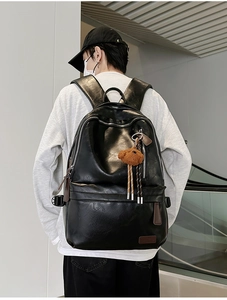 Detail of black leather commuter backpack featuring silver zippers and a plush bear charm
