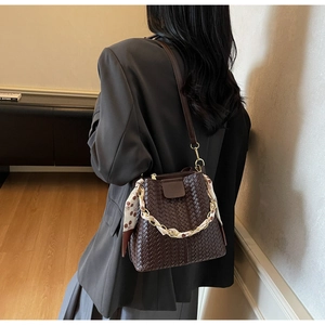 Détail d'un sac seau tressé marron foncé avec foulard en soie porté par un mannequin
