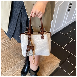 Detail of light gray textured bucket bag with dark brown knotted handle and bow charm