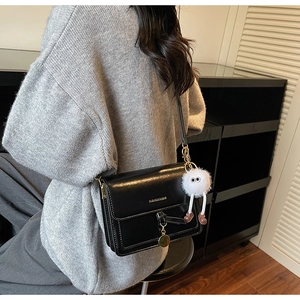 Detail of black crossbody bag with gold hardware and a white monster fur ball charm