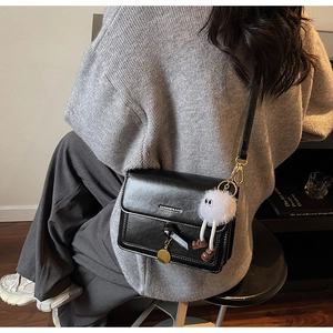 Chic black crossbody bag detail with metallic lettering and cute plush doll pendant