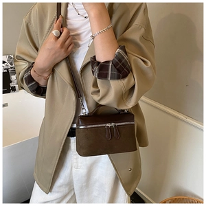 Détail d'un sac bandoulière en daim marron avec double fermeture éclair et finitions métal