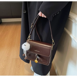Detail of dark brown glossy leather crossbody bag with knot decor and golden charm