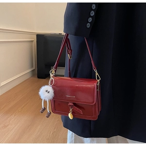 Close-up of burgundy crossbody bag with fur charm and gold circular pendant detail