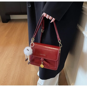 Detail of burgundy PU leather crossbody bag with metal pendant and plush charm on black coat
