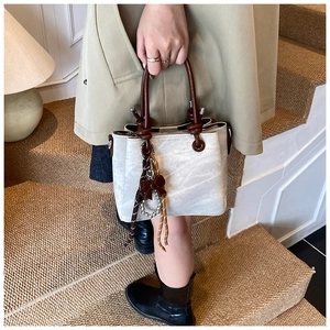 Detail of vintage white bucket bag with dark brown knotted handles and tassel charm
