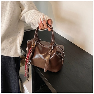 Detail of dark brown faux leather Boston bag featuring woven tassel zipper charms