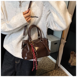 Detail of glossy dark brown Boston handbag with shiny finish and woven ribbon charm