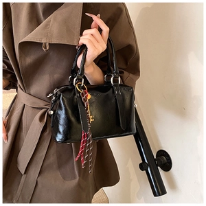 Close-up of black glossy handbag with golden key charm and striped rope detail
