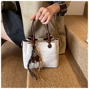 Close-up of beige textured leather bucket bag with brown handles and decorative tassels