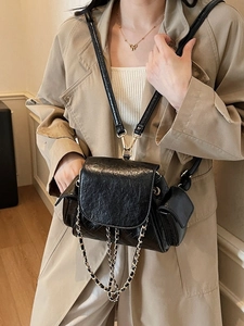 Quilted black patent leather shoulder bag with gold chains shown on a model in a beige trench coat