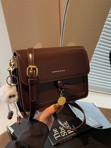 Minimalist deep brown crossbody bag in matte leather with golden logo and plush charm