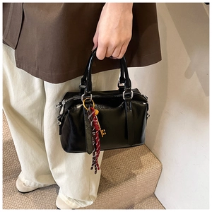 Detail of black patent leather Boston bag featuring a metal key charm and woven tassels