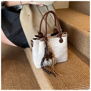 Close-up of cream bucket bag with brown circular handle and decorative tassel on stairs