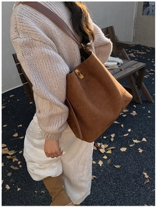 Brown suede bucket bag with gold twist lock and wide shoulder strap shown in a lifestyle scene