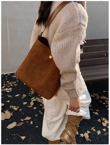 Close-up of brown suede bucket bag featuring elegant gold metal hardware and strap