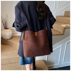 Detail view of large brown suede bucket bag with elegant gold twist lock and shoulder strap