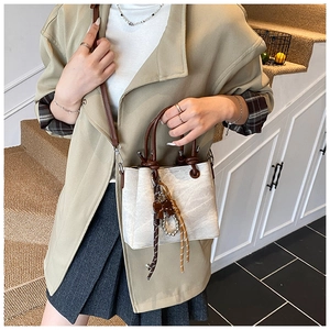 Detail of cream canvas bucket bag with brown leather handles and pearl tassel charms
