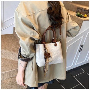 Model wearing a minimalist cream bucket bag with brown handles and bow charm detail