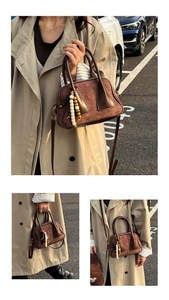 Detail of a brown suede Boston bag featuring unique beaded charms and leather handles