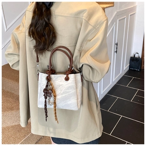 Lifestyle shot of an off-white canvas bucket bag with brown leather handles and charm