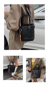 Close-up of black bucket bag featuring woven wooden bead pendant and adjustable strap
