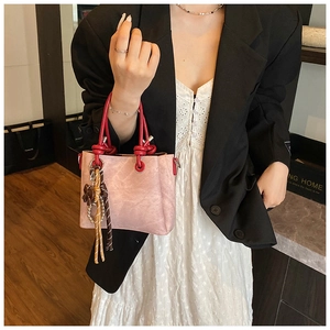Pink bucket bag with red knotted handles and tassel charm shown on a female model