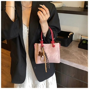 Detail of pink faux suede bucket bag with bright red ring handle and bow accessory