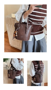 Detail of dark coffee bucket bag featuring wood bead pendant and adjustable metal buckle