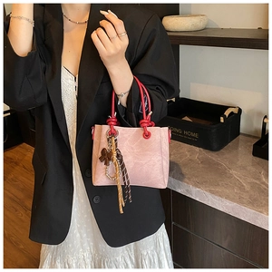 Detailed shot of pink faux suede bucket bag featuring red knot handle and pearl chain