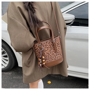 Leopard print bucket bag with brown leather strap worn by a model in outdoor setting