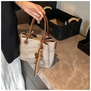 Detail view of beige leather bucket bag featuring a woven rope handle and heart pendant