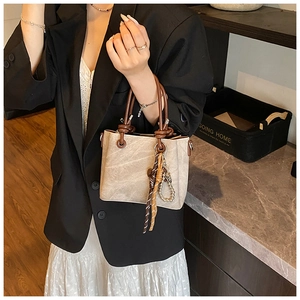 Detail of vintage beige bucket bag with dark brown ring handles and woven tassel charm