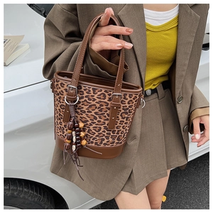 Detail view of leopard print bucket bag featuring wooden bead tassel and brown leather trim
