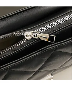Macro shot of silver metallic zipper pull and black quilted leather texture on crossbody bag