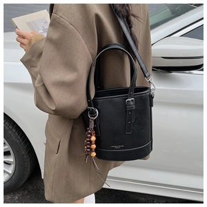 Detail of a black minimalist bucket bag with leather texture and wooden bead pendant accessory