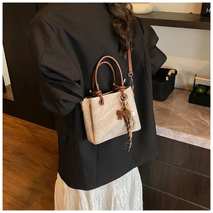 Detail of beige bucket bag with brown handles and a decorative bow charm on a model