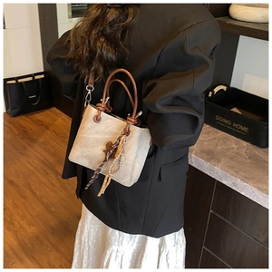 Beige bucket bag with brown handle and pearl charm shown on a person in home setting