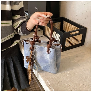 Detail of light blue washed texture handbag with brown leather handles and bow charm