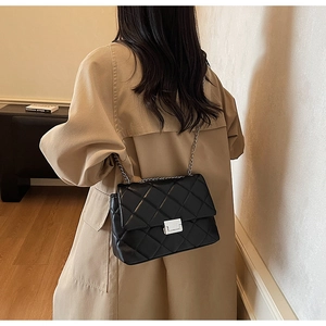 Detailed view of black quilted crossbody bag featuring silver chain and lock closure
